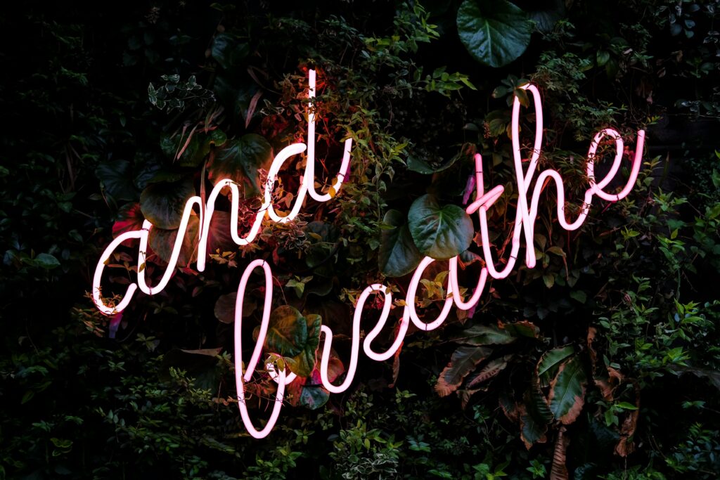 Neon "and breath" sign on leafy green backdrop.