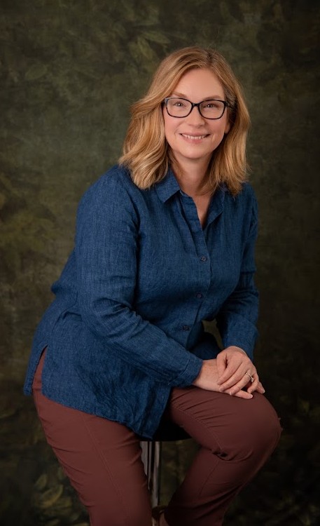 Professional photo of Colleen Godfrey smiling, seated on director's chair with hand on knee